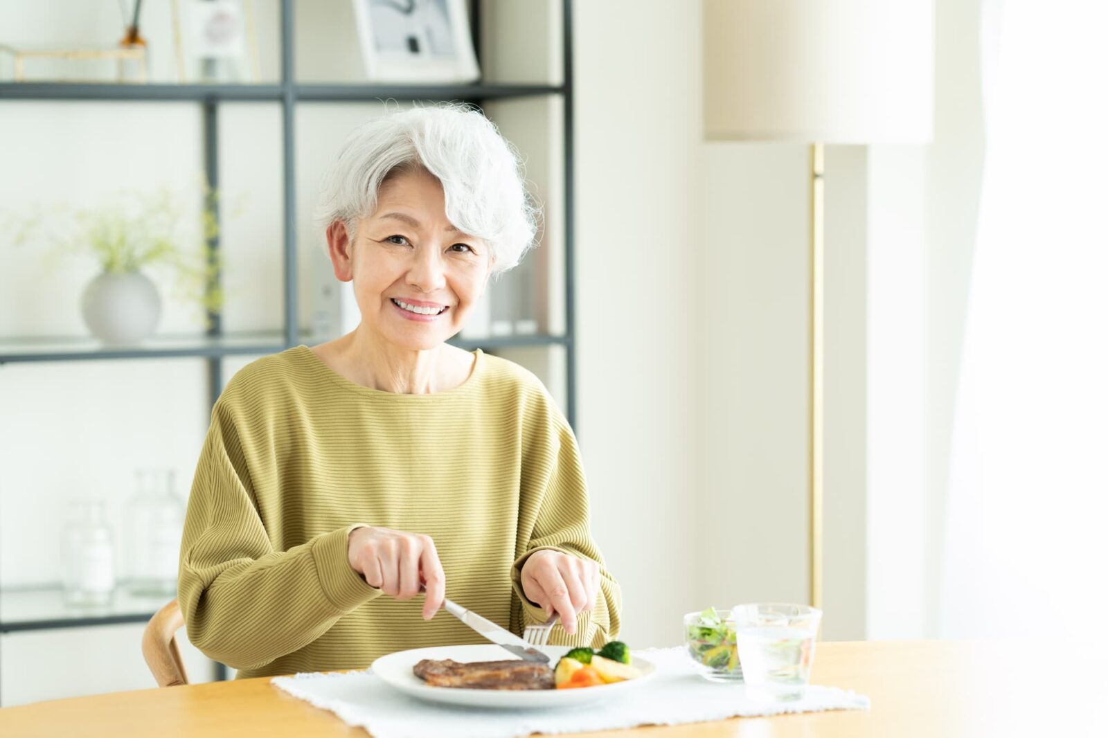 入れ歯の痛みが無くなり美味しくステーキを食べるシニア女性