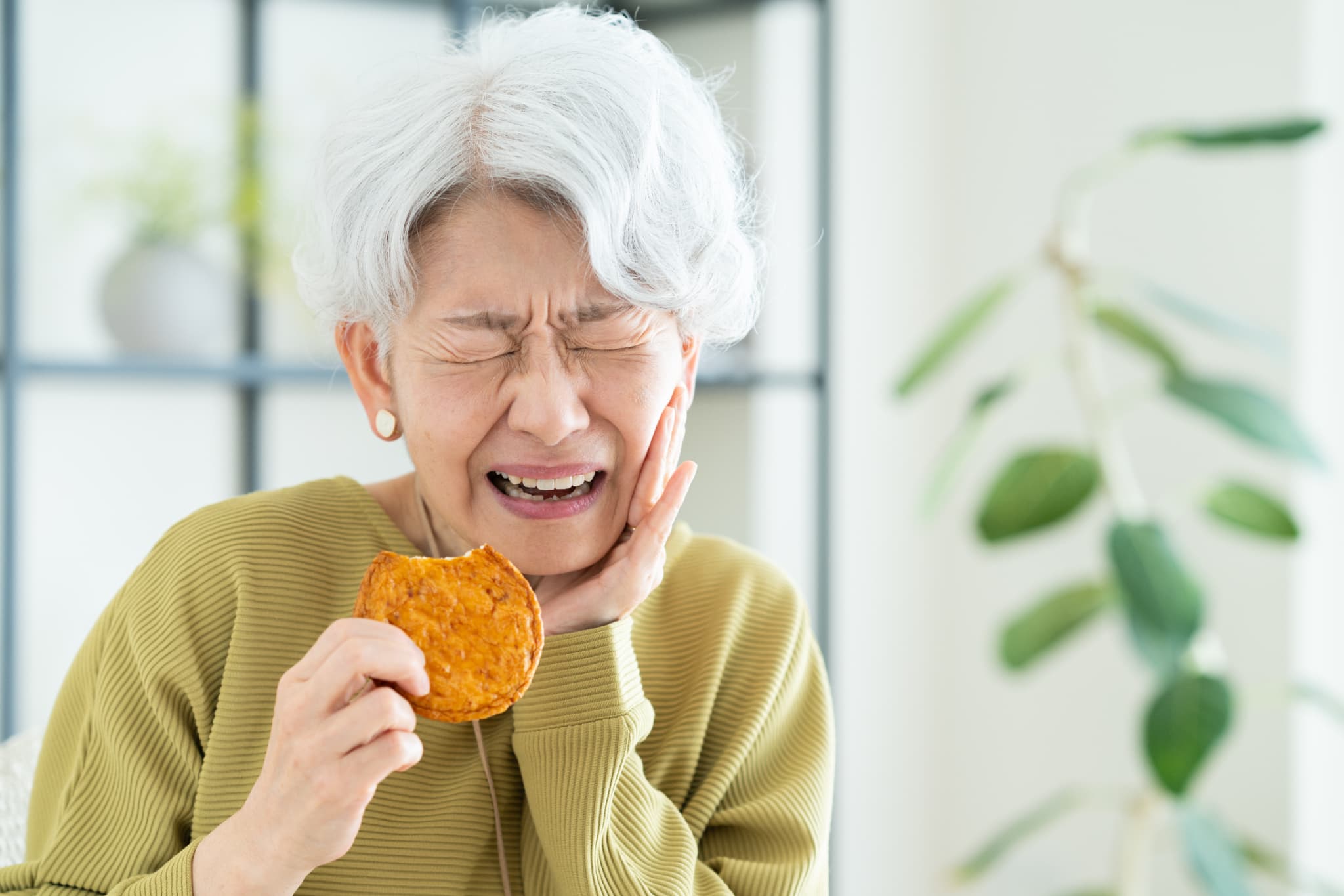 硬いせんべいを食べて入れ歯が痛む女性